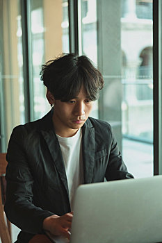 一名亚洲男子在咖啡馆使用笔记本电脑加班