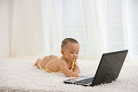 趴在地毯上玩电脑的婴儿