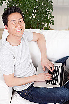 一个坐在白色沙发上用笔记本电脑的青年男士