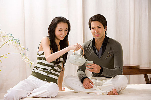 一对年轻夫妻坐在床上喝茶