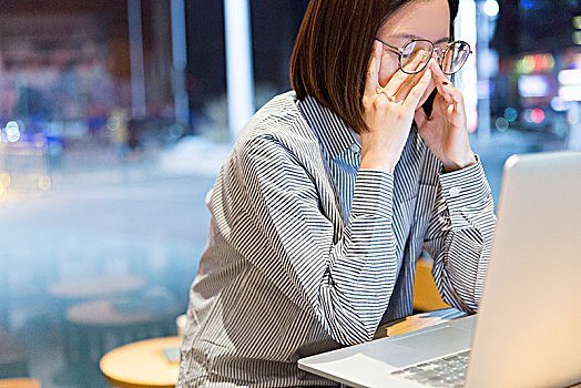 年轻的女性在咖啡馆中工作,坐在笔记本电脑前揉眼睛