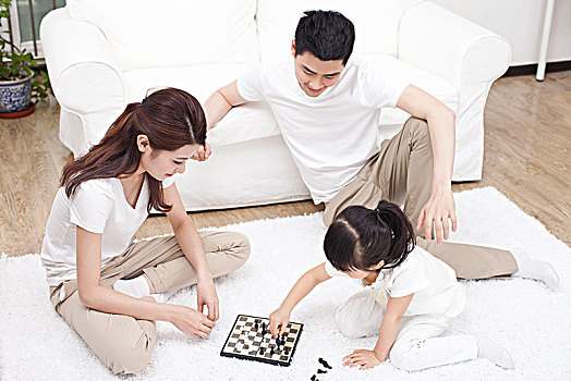 三口之家围坐在地毯上玩国际象棋
