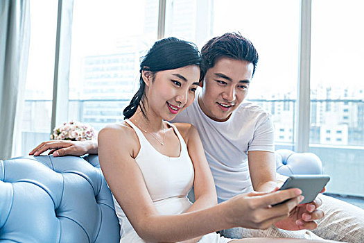 年輕情侶在沙發(fā)上使用手機(jī)