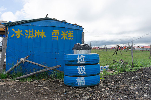 草原上路边人工搭建的蓝屋子和轮胎做的创意蓝色垃圾桶