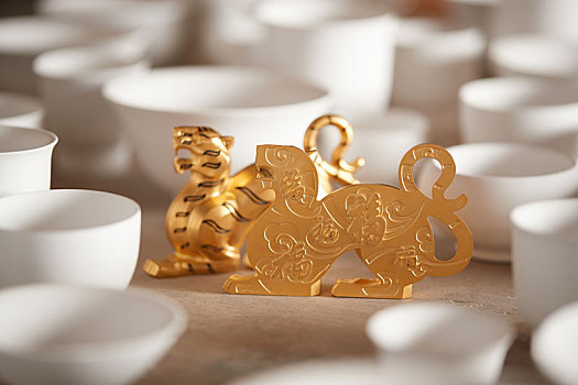 带有福字的金色老虎摆件在各式白色茶碗中浅色实木桌面