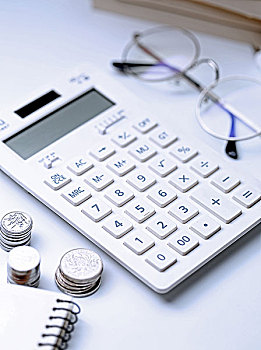 计算器硬币和钢笔放在白色桌面上