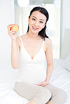 坐在床上拿苹果的孕妇