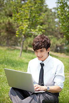 坐在草坪上看电脑的男青年