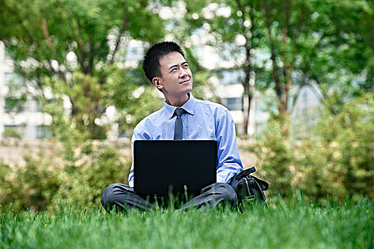 坐在草地上拿电脑的商务男士