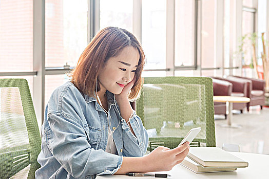 在图书馆看玩手机,听音乐的女大学生