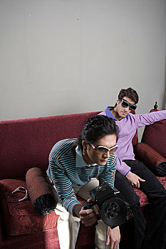 两位先生拿着摄像机坐在沙发上休息