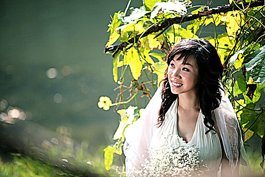 身着白色婚纱的年轻女子站在树荫下