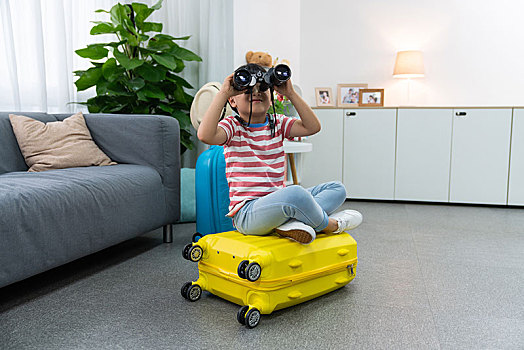 快乐的小男孩拿着望远镜坐在行李箱上