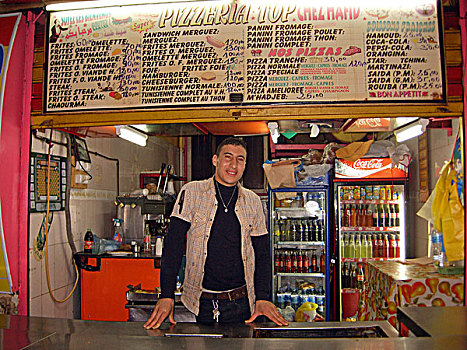 algeria,alger,man,in,casual,clothing,standing,by,counter,the,restaurant,with,refrigerator,filled,of,bottles,soft,drink,background