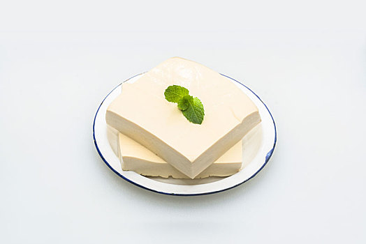两块豆腐盛在盘子里,绿色薄荷叶点缀,放在白色背景上