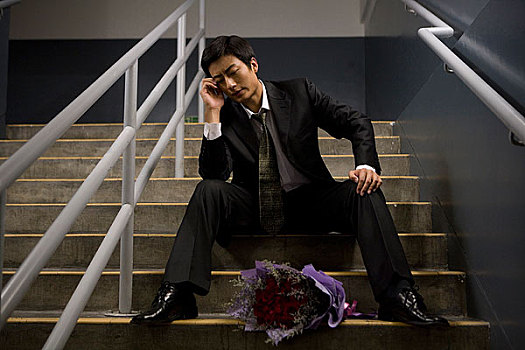 坐在建筑台阶上手捧鲜花等人的男士