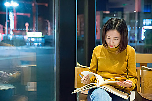 夜晚在咖啡馆靠窗翻阅书籍的女性