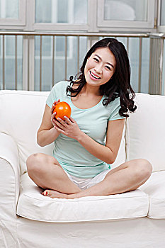 年轻女士坐在沙发上拿着橙子