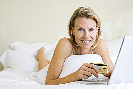 女人,卧,床上,使用笔记本,拿着,信用卡,看镜头,微笑