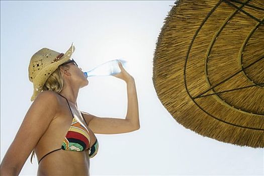 女人,站立,靠近,海滩伞,喝,水瓶