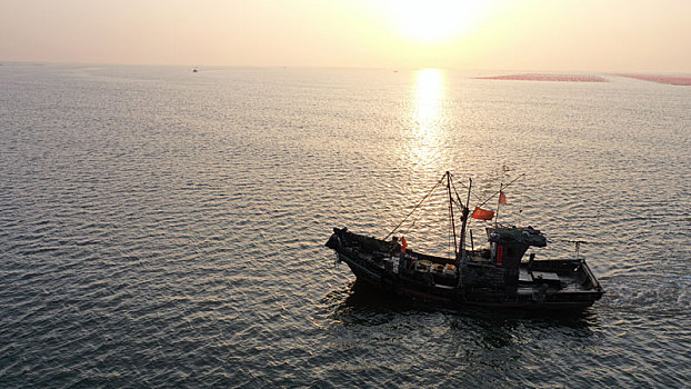 渔民迎着金色阳光,在广阔大海中耕海牧渔