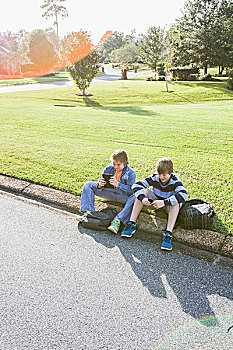两个男孩,坐,居民区,路边,手持,电子产品