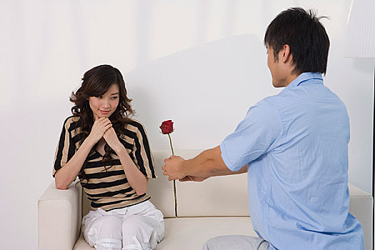 一个男人拿着一支花向坐在沙发上的女人求婚