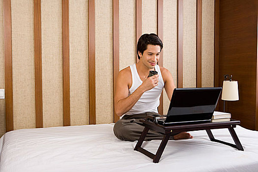 一个男人坐在床上玩电脑