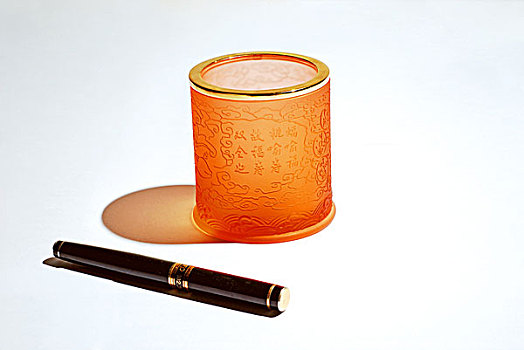 一个橘色玻璃笔筒和钢笔