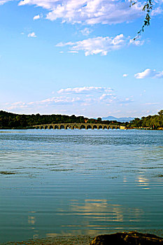颐和园的昆明湖上倒映着白云和远处的十七孔桥