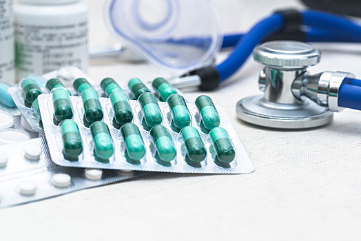 绿色胶囊在桌上,虚化的听诊器,药瓶,药品与医疗用品