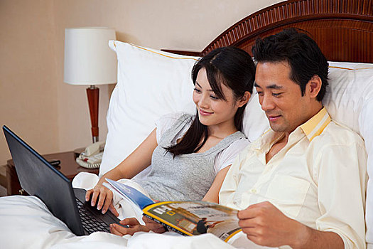 夫妻躺在床上看杂志使用电脑