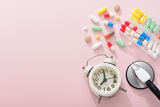 粉色背景上的药片,闹钟和听诊器