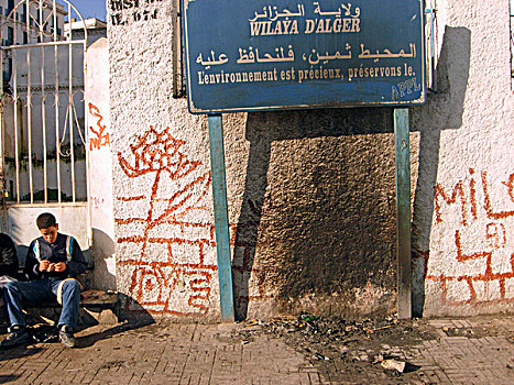 algeria,alger,commercial,sign,displayed,in,front,of,wall,with,graffiti,while,a,boy,sitting,closed,metal,gate