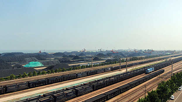 山东省日照市,蓝天下的港口煤炭堆场整齐划一,火车满载货物铿锵前行