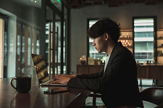一名亚洲男子在咖啡馆使用笔记本电脑加班
