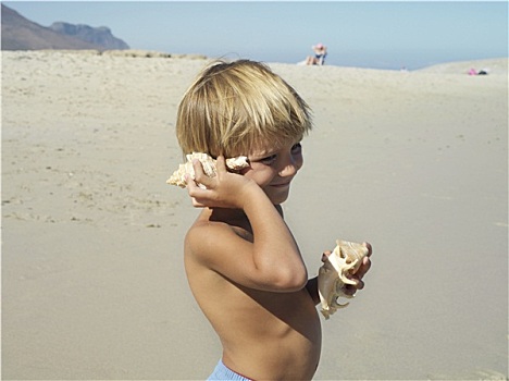 金发,男孩,5-7岁,站立,海滩,听,海洋,壳,微笑,侧面视角