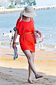 穿着粉色连衣裙漫步在海边沙滩上的女人