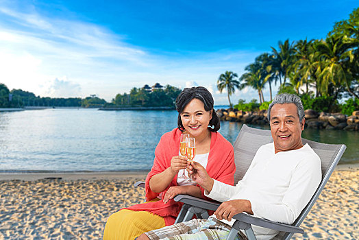快乐的老年夫妇坐在沙滩椅上喝香槟酒