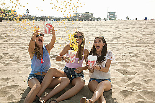 三个女人,年轻,坐,海滩,投掷,爆米花,空中