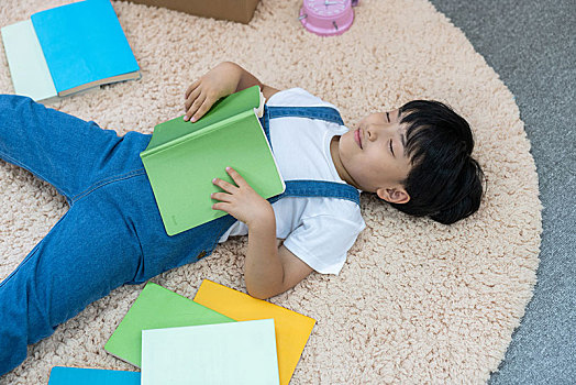 快乐的小男孩躺在地毯上看书