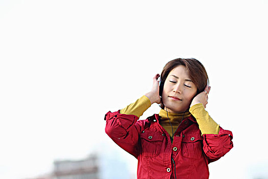 女人,听歌头戴耳机闭着眼睛听音乐的年轻女人一个时尚女人走过上海