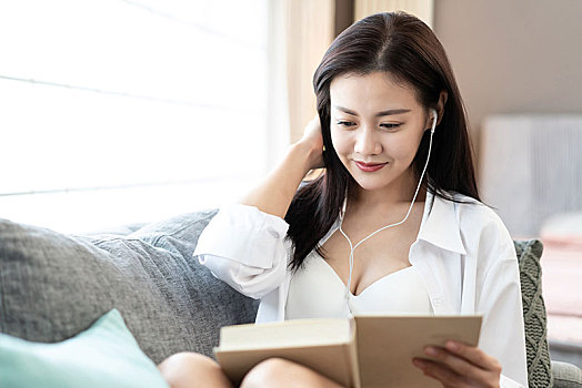年轻女子在沙发上看书听音乐