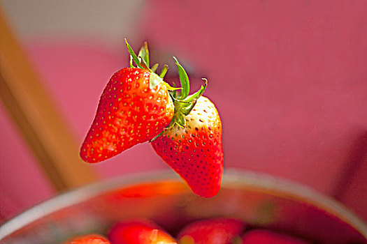 两个新鲜红色的草莓悬在半空中的特写
