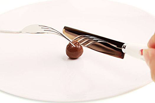 在白色盘子里用银色刀叉切开圆形棕色巧克力