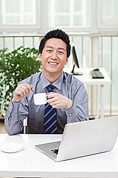 一个在办公室喝咖啡用电脑的青年商务男士