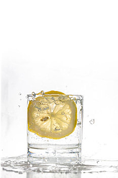 一片新鲜的柠檬片掉入玻璃水杯中的瞬间水花飞溅空中