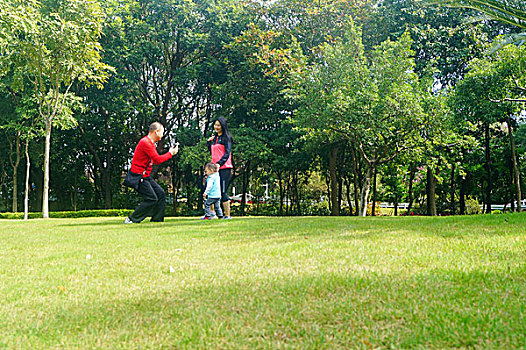 年輕夫婦帶著孩子在公園草坪上拍照