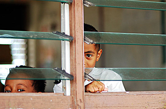 tuvalu,funafuti,schoolboys,in,classroom,looking,through,glass,shutters,one,playful,boy,winking