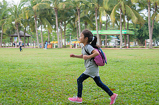 背着包在草地上奔跑的小女孩